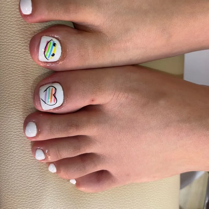 White pedicure with rainbow heart art by LENA Nails & Beauty, nail salon in Da Nang