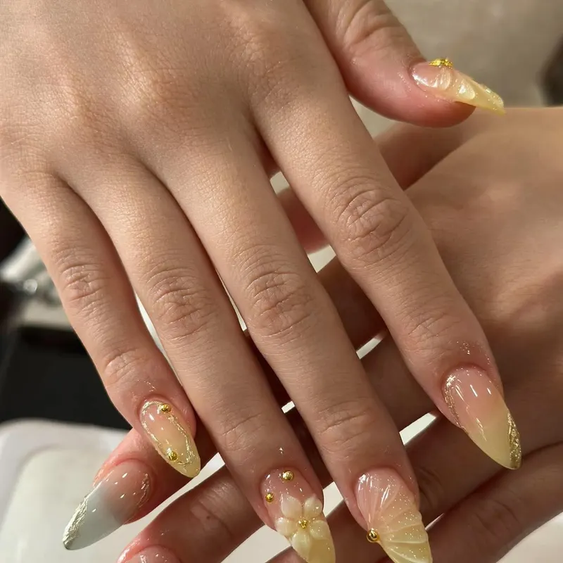 Almond nails with gold glitter ombre and flower charm by LENA Nails & Beauty, nail salon in Da Nang